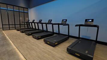A row of treadmills with digital displays, a wooden floor, and a blue wall with a decorative screen.