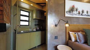 Une petite cuisine avec une fenêtre, un évier et une cuisinière. Un lampadaire fixé au mur et une plante en pot encadré ornent le mur.