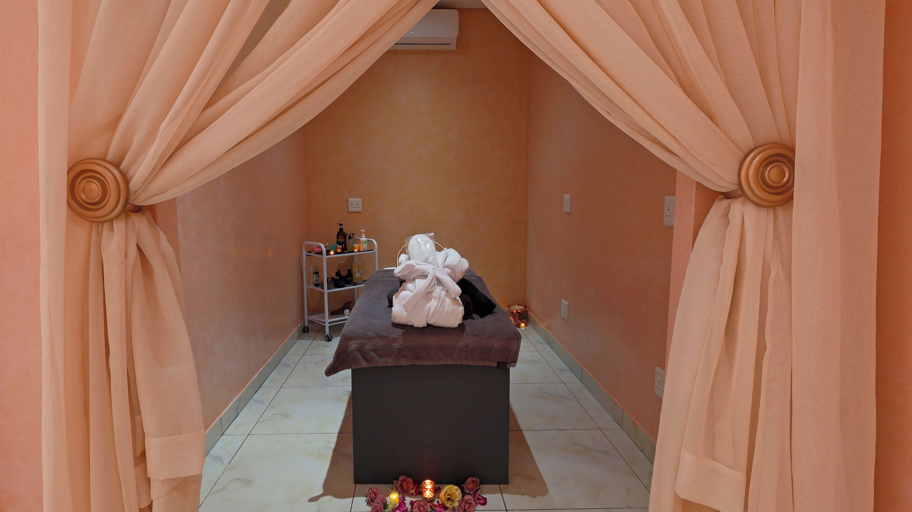 Ein Wellnessraum mit Massageliege, Handtüchern und einem Ablagefach für Toilettenartikel.