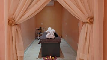 A spa room with a massage table, towels, and a shelf with toiletries.