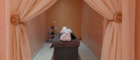 A spa room with a massage table, towels, and a shelf with toiletries.