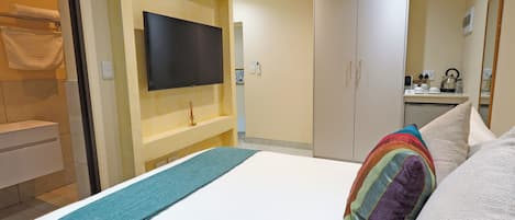 Une chambre d’hôtel comprenant un lit, un téléviseur fixé au mur, une armoire et un petit coin cuisine.