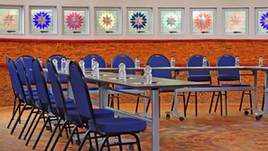 A conference room with a brick wall, blue chairs, tables with water bottles, and colorful stained glass windows. - Qurtuba Resort And Events (Johannesburg)