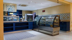 A bakery counter with a display case, a refrigerator, and a digital clock. - Qurtuba Resort And Events (Johannesburg)