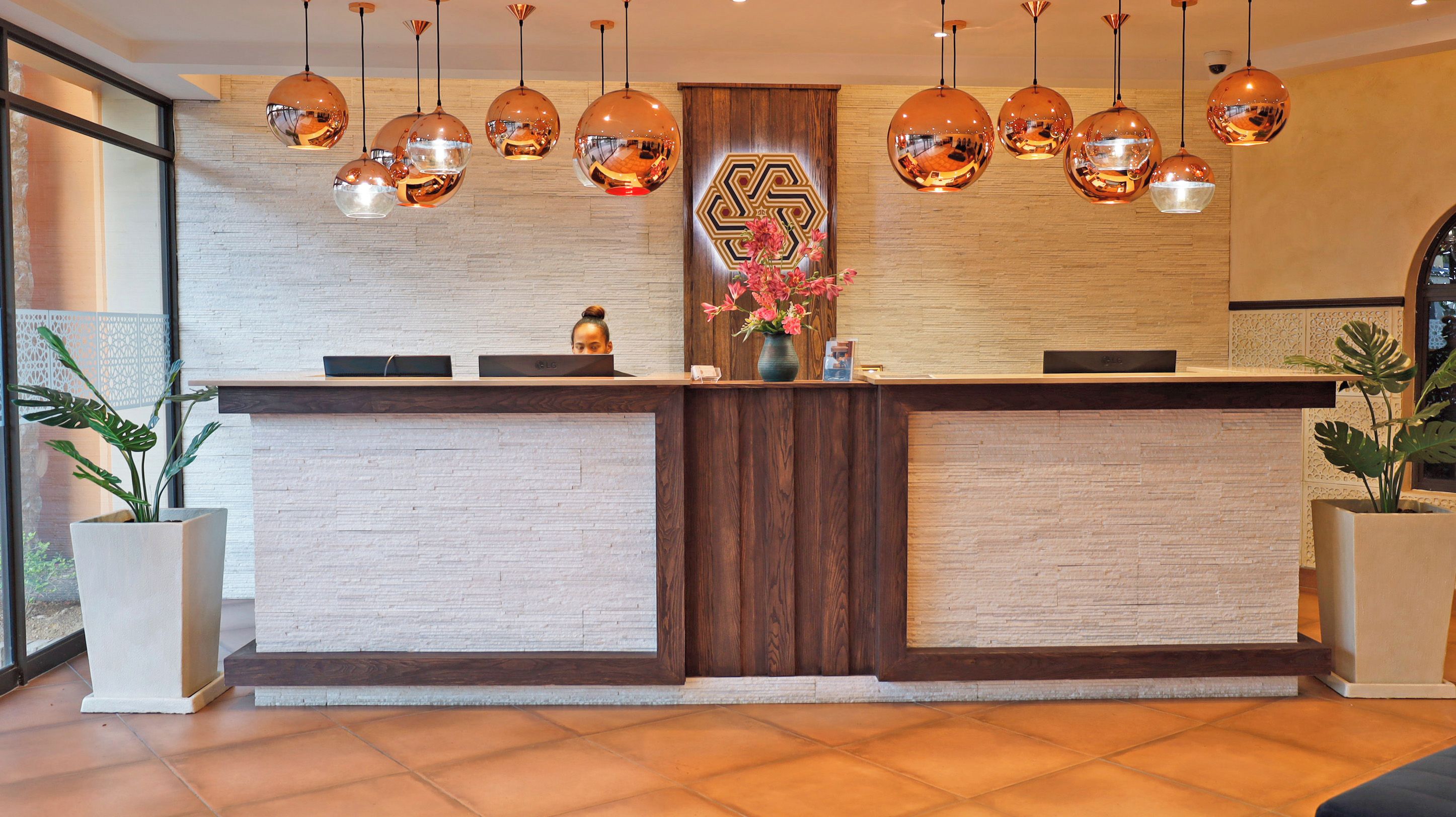 A reception desk with a wooden finish, a large decorative wall piece, and multiple spherical pendant lights.