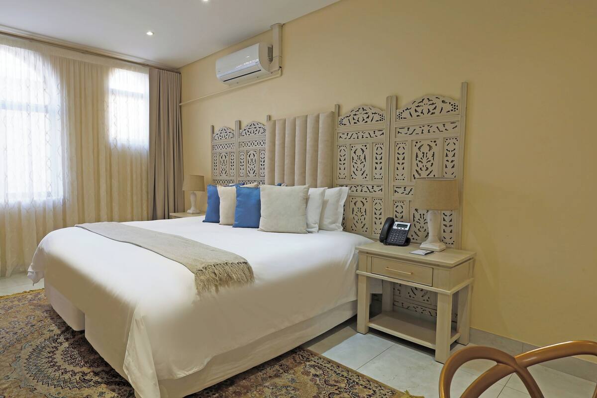 Camera d'albergo con un letto grande, un comodino con telefono e lampada, e una testiera decorativa.