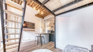 Una cuina moderna amb taulell de fusta, un frigorífic i un microones. Hi ha una escala de fusta recolzada contra la paret i una taula rodona blanca al primer pla.