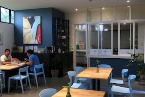 Interior de restaurante con mesas y sillas, un cuadro abstracto grande en la pared y una ventana con vistas.
