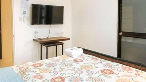 A hotel room with a bed, a TV mounted on the wall, a small table, and a window. - RedDoorz @ Occazia Hotel Pampanga (Bacolor)
