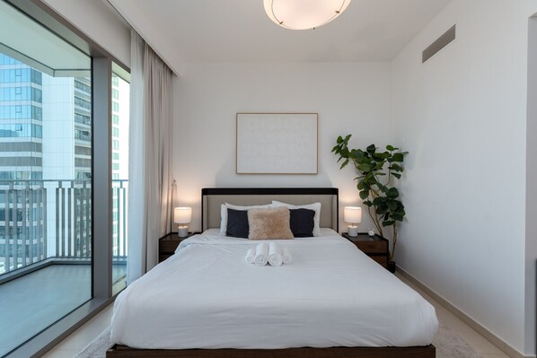 A modern hotel room with a large bed, a view of the city, and a potted plant.