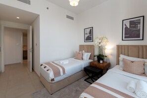 A hotel room with two beds, a bedside table with a lamp, a potted plant, and framed pictures on the wall.