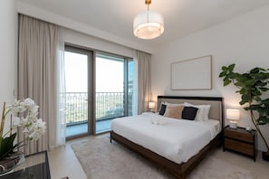 Une chambre moderne avec un grand lit, une porte vitrée donnant sur un balcon, une table de chevet avec une lampe et une plante en pot.