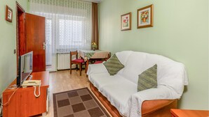 A cozy living room with a white sofa, a wooden side table with a telephone, a small table with a vase, and a window with sheer curtains. - Amazing apartment in Palit with house sea view (Palit)