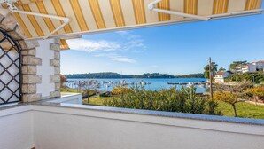 A balcony with a view of a marina and boats, stone wall, and a striped awning. - Amazing apartment in Palit with house sea view (Palit)