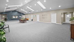 A spacious room with a high ceiling, recessed lighting, and a central table with chairs.
