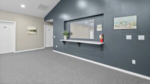 A hallway with a dark grey wall, a white door labeled '15', a small shelf with a plant, and a framed picture.