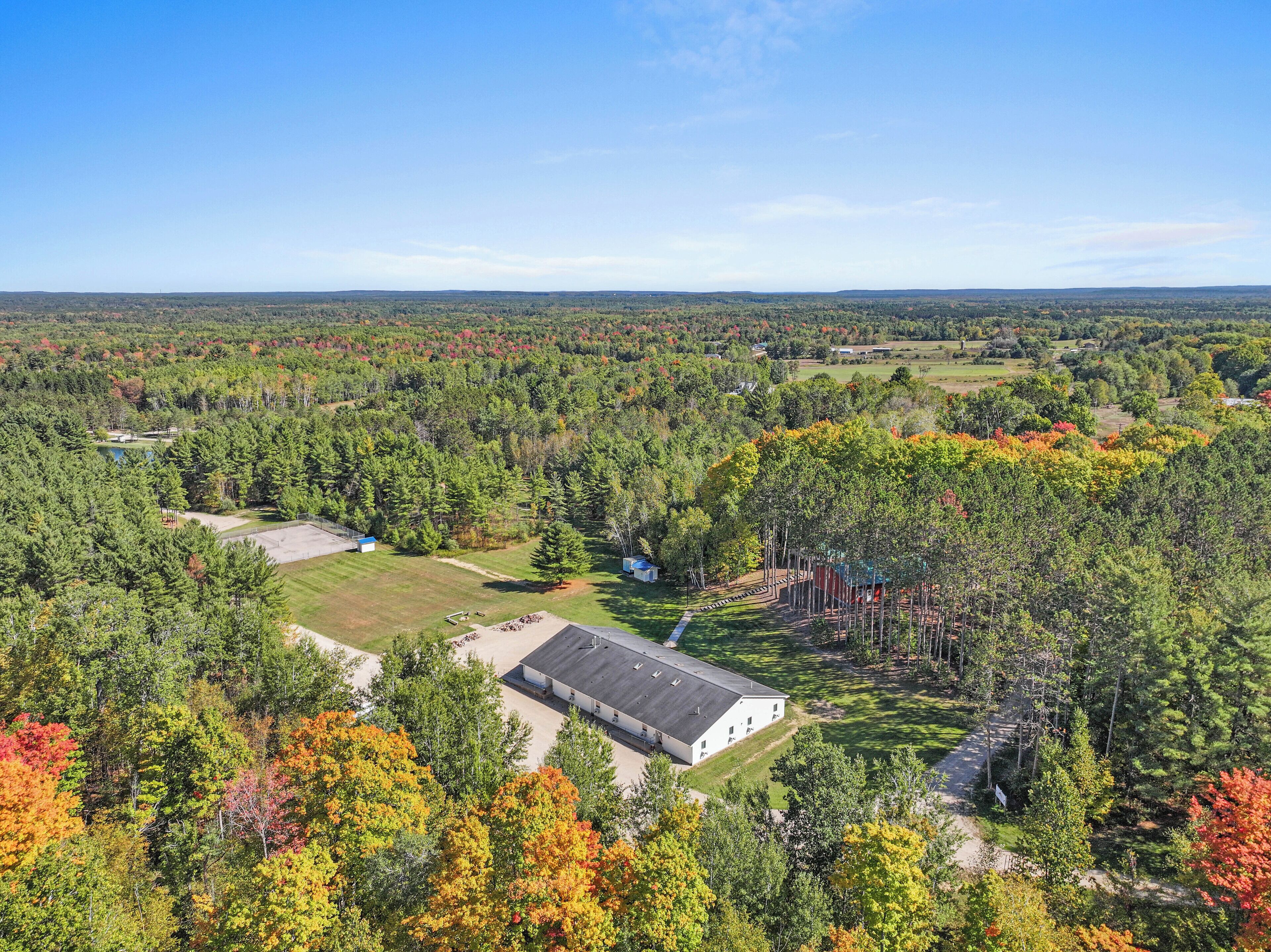 An aerial view of a property with a large building, a pond, and a forested area.