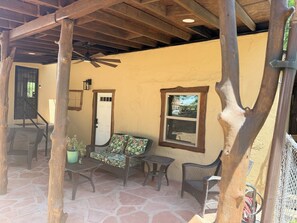A covered patio area with wicker furniture, a ceiling fan, and a stone floor.