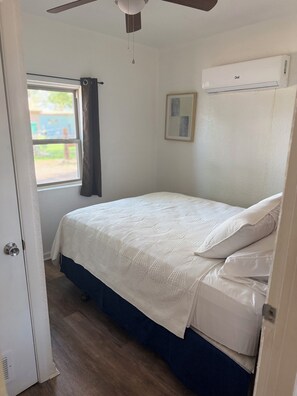 A bedroom with a bed, a window with curtains, a ceiling fan, and an air conditioning unit. - Huerta Cottage - Historic Farm Cottage (El Paso)