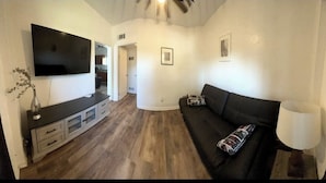 Un salon avec un téléviseur à écran plat, un canapé foncé, une lampe et un plancher en bois.