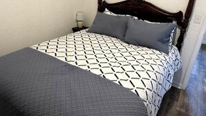 Un lit avec une couvre-lit à motifs géométriques, une tête de lit en bois et une table de chevet avec une lampe.