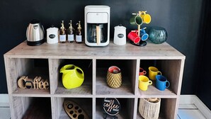 A wooden coffee station with a painting of a house and palm trees on the wall behind it.