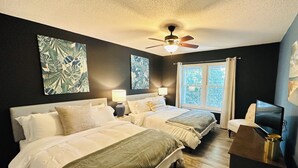 A hotel room with two beds, a ceiling fan, a window with curtains, and a TV on a stand.