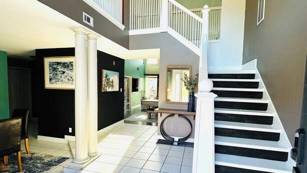 A spacious interior with a staircase leading to an upper level, tiled floors, and a dining area with chairs and a table.