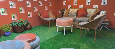 A cozy indoor seating area with wicker furniture, artificial grass flooring, and potted plants.