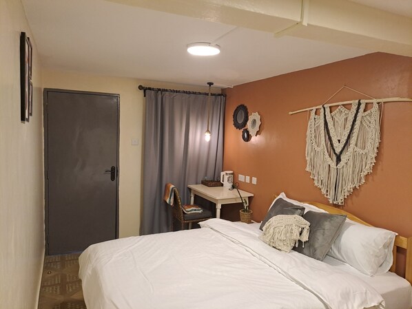 Habitación de hotel con cama, escritorio, silla y una decoración de macramé en la pared, además de una puerta.