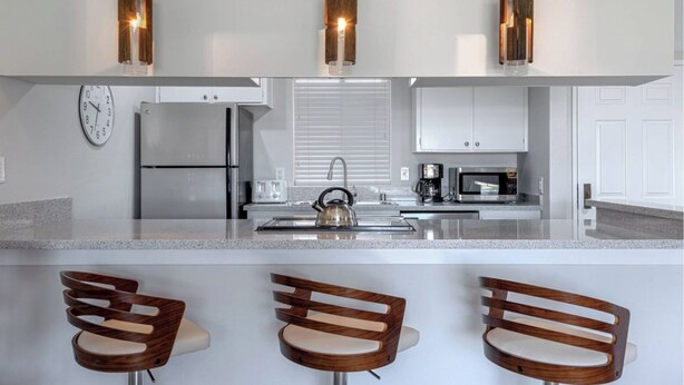 Een moderne keuken met een centraal eiland, roestvrijstalen apparatuur en houten barstoelen.