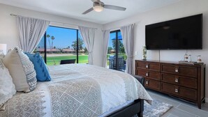 Een slaapkamer met een groot bed, een plafondventilator, een televisie en uitzicht op een golfbaan.