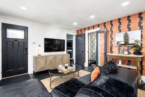 Ein modernes Wohnzimmer mit einer schwarzen Couch, einem Glastisch und einem an der Wand befestigten Fernseher.