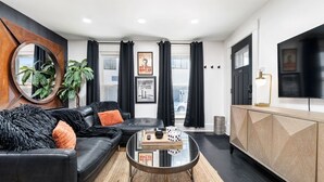 Un salon moderne avec un canapé en cuir noir, une table basse en verre et un meuble en bois.