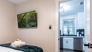 Ein Schlafzimmer mit einem Bett, einem Deckenventilator, einem Fernseher und einem Waldgemälde.