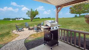 A covered outdoor area with a barbecue grill, seating, and a view of a green field.