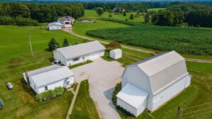 A large, white, single-story building with a flat roof, surrounded by green fields and trees.