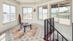 A sunlit room with a view of a pool and a balcony, featuring a wooden table, ottomans, and a patterned floor. - Whirlwind Waters Paradise (Russells Point)