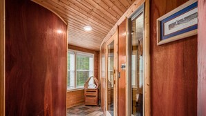 A wooden hallway with a tiled floor, a window with blinds, a small wooden bench, and a framed picture on the wall. - Whirlwind Waters Paradise (Russells Point)