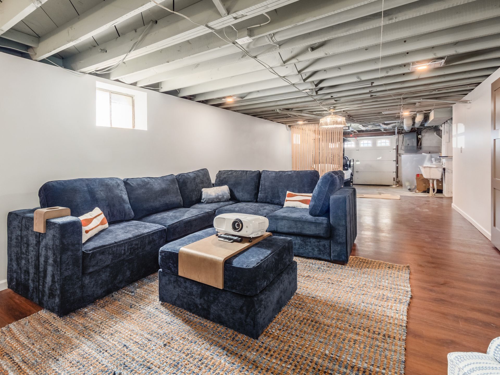 Ein modernes Wohnzimmer mit einem dunkelblauen Ecksofa, einem Couchtisch mit Projektor und einem großen Fenster, das natürliches Licht hereinlässt.