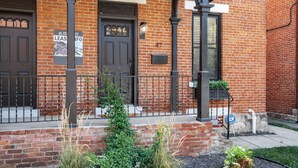 A brick building with a dark brown door, a sign for 'SHOW LUXURY LEASING', and a small garden area with plants. - The Pop Fusion Pad in Short North (Columbus)