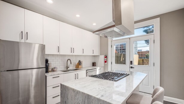 A modern kitchen with white cabinets, a stainless steel refrigerator, a marble countertop, and a gas range. - The Pop Fusion Pad in Short North (Columbus)