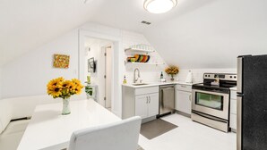 A modern kitchen with white cabinetry, a black refrigerator, and a dining area with a white table and chair.