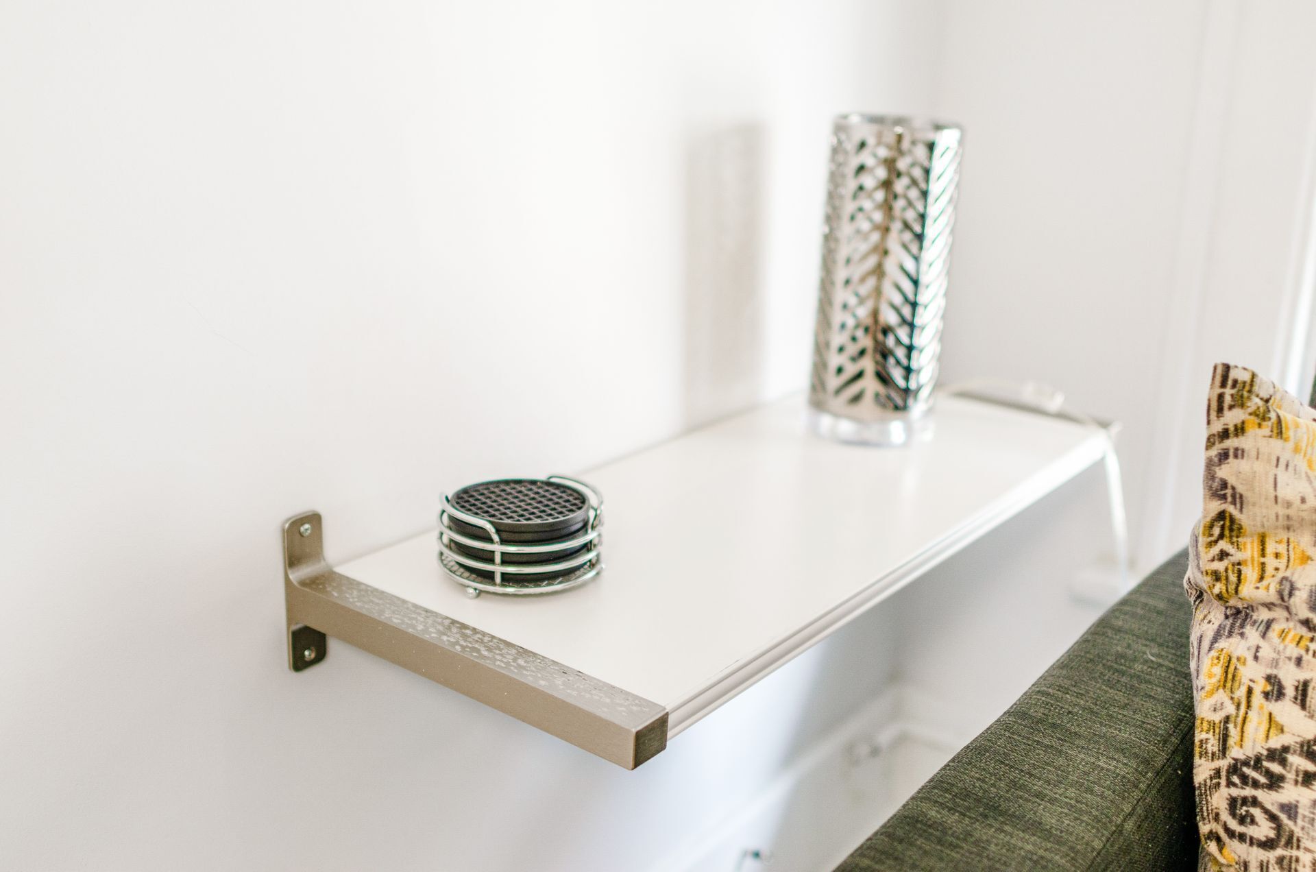 Une étagère blanche avec un support métallique, une pile de dessous-de-verre et un vase décoratif.
