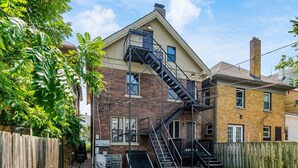 A two-story house with a brick exterior, a black fire escape, and a wooden fence.