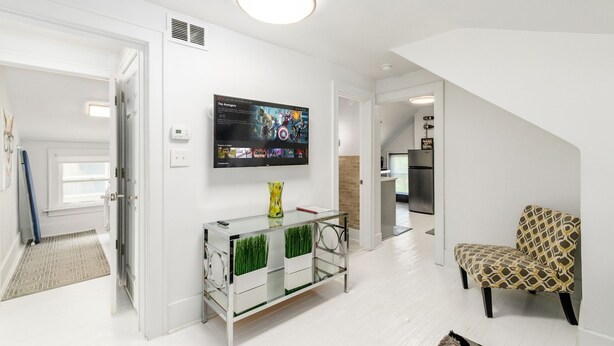 A modern living room with a flat-screen TV, a glass coffee table with a vase, a patterned armchair, and a staircase leading to another level.