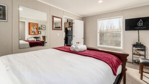 Ein Hotelzimmer mit einem großen Bett, einem Fernseher, einem Fenster mit Blick auf Bäume und einer Küchenzeile.