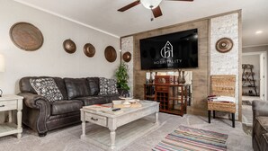 Ein Wohnzimmer mit Ledersofa, Couchtisch, Wand-Fernseher und Deckenventilator.