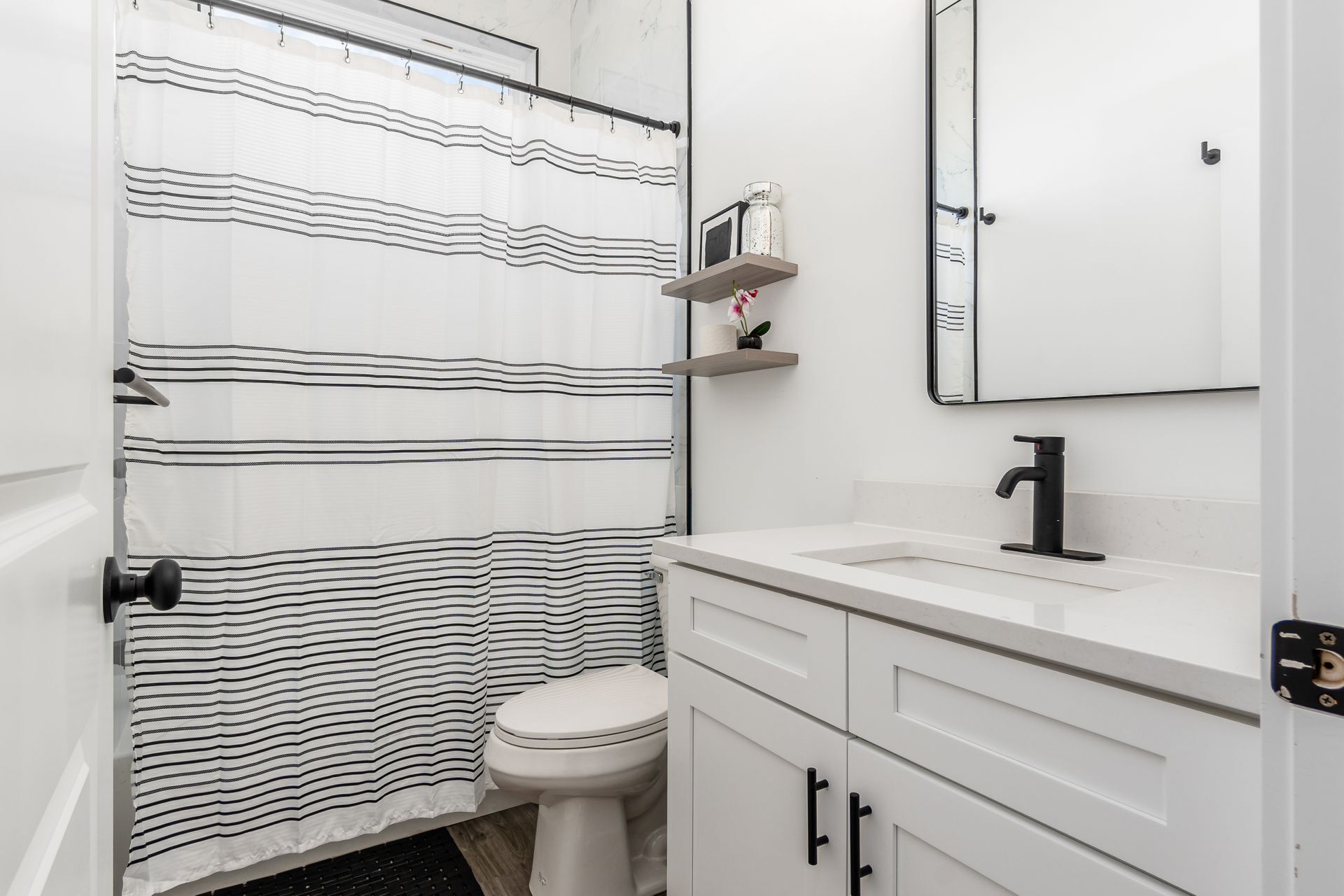 A bathroom with a striped shower curtain, a toilet, a white sink with a black faucet, and a mirror above the sink.