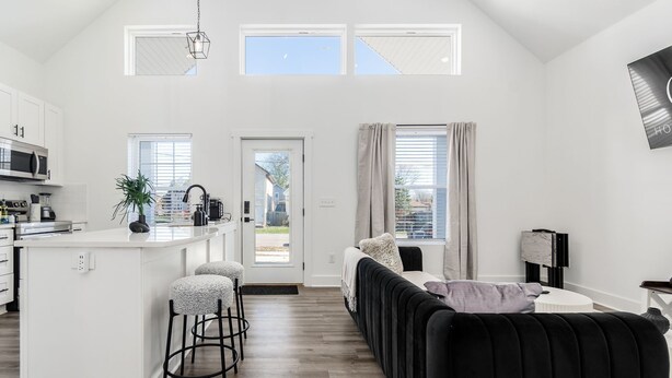 Una cocina moderna con armarios blancos, una isla central con taburetes, un sofá negro y una mesa de comedor.